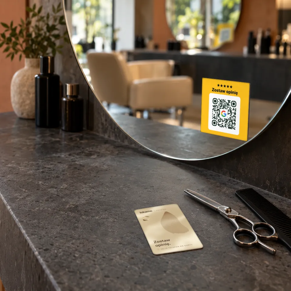 Stanowisko fryzjerskie: karta NFC Lokamo na kamiennym blacie obok nożyczek, naklejka QR na okrągłym lustrze.